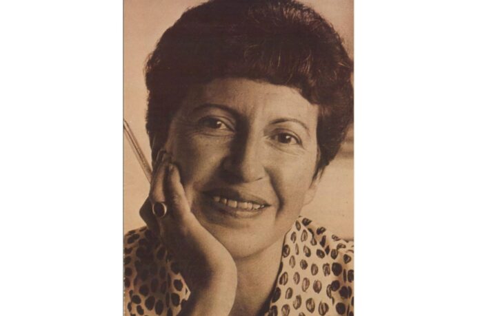 azra erhat elinde kalem ile gülümsemektedir